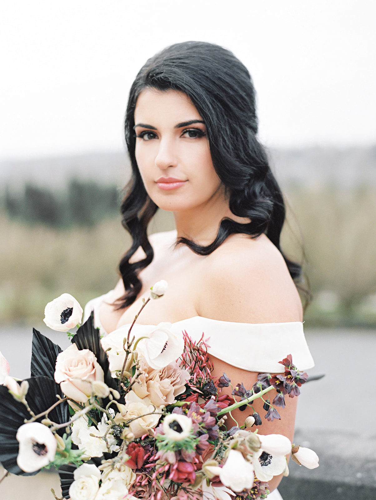 Chateau-Lill-Wedding-Bouquet-Details.jpg A bride holding a bouquet with anenomes, spring tulips and fritillaria, blooming branches, roses, and black palm spears