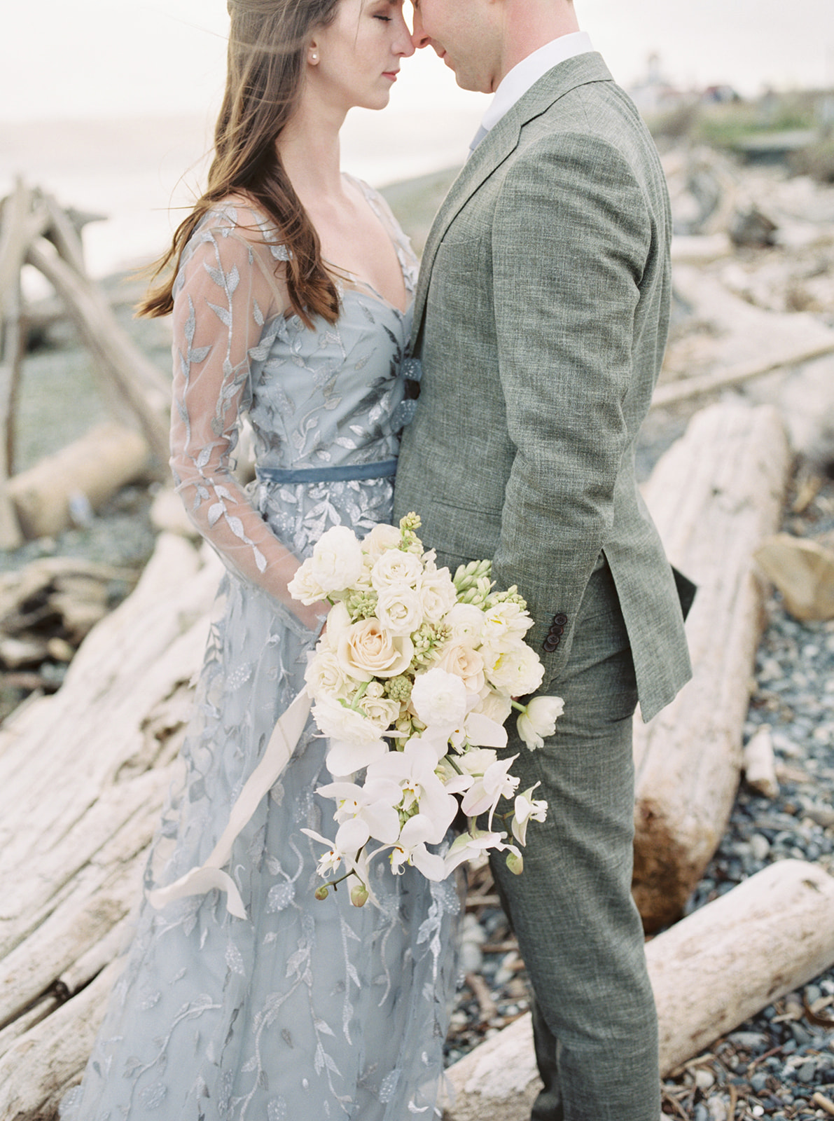 Discovery-Park-Elopement-Emrbacing-in-Front-of-Driftwood.jpg Couple standing in front of driftwood, holding bouquet