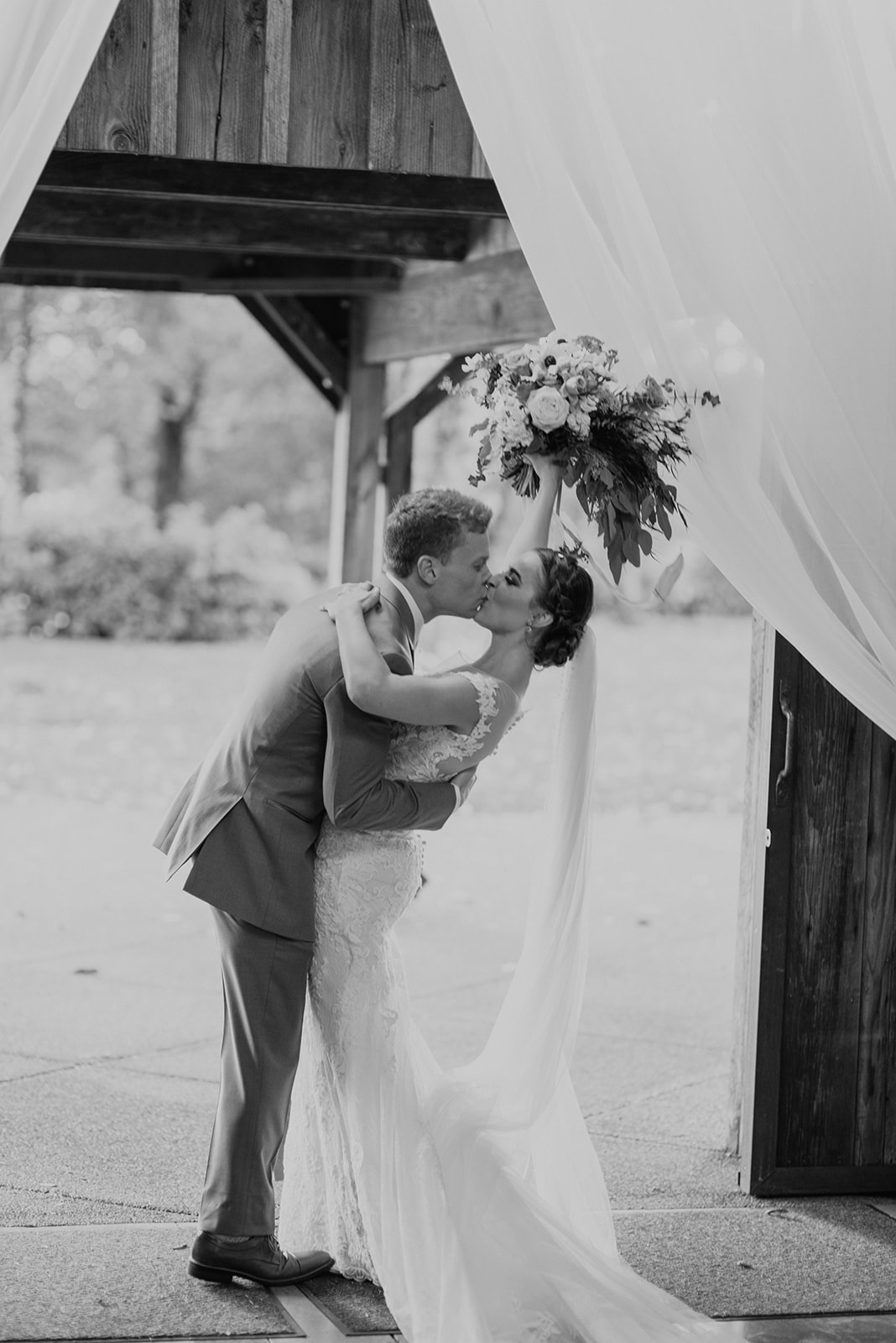 Kelley-Farm-Wedding-Bouquet-Up-High.jpg A black and white image of the bouquet being held high while couple kisses