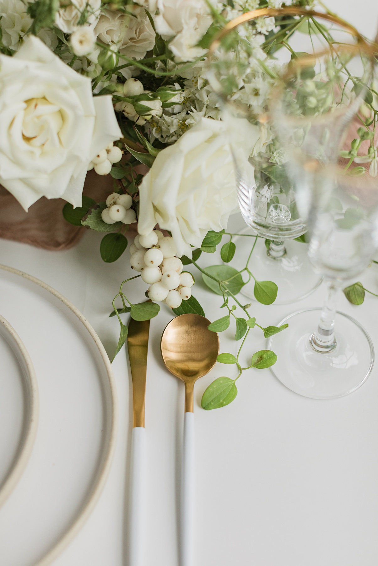 A place setting with gold silverware and white floral centerpiece