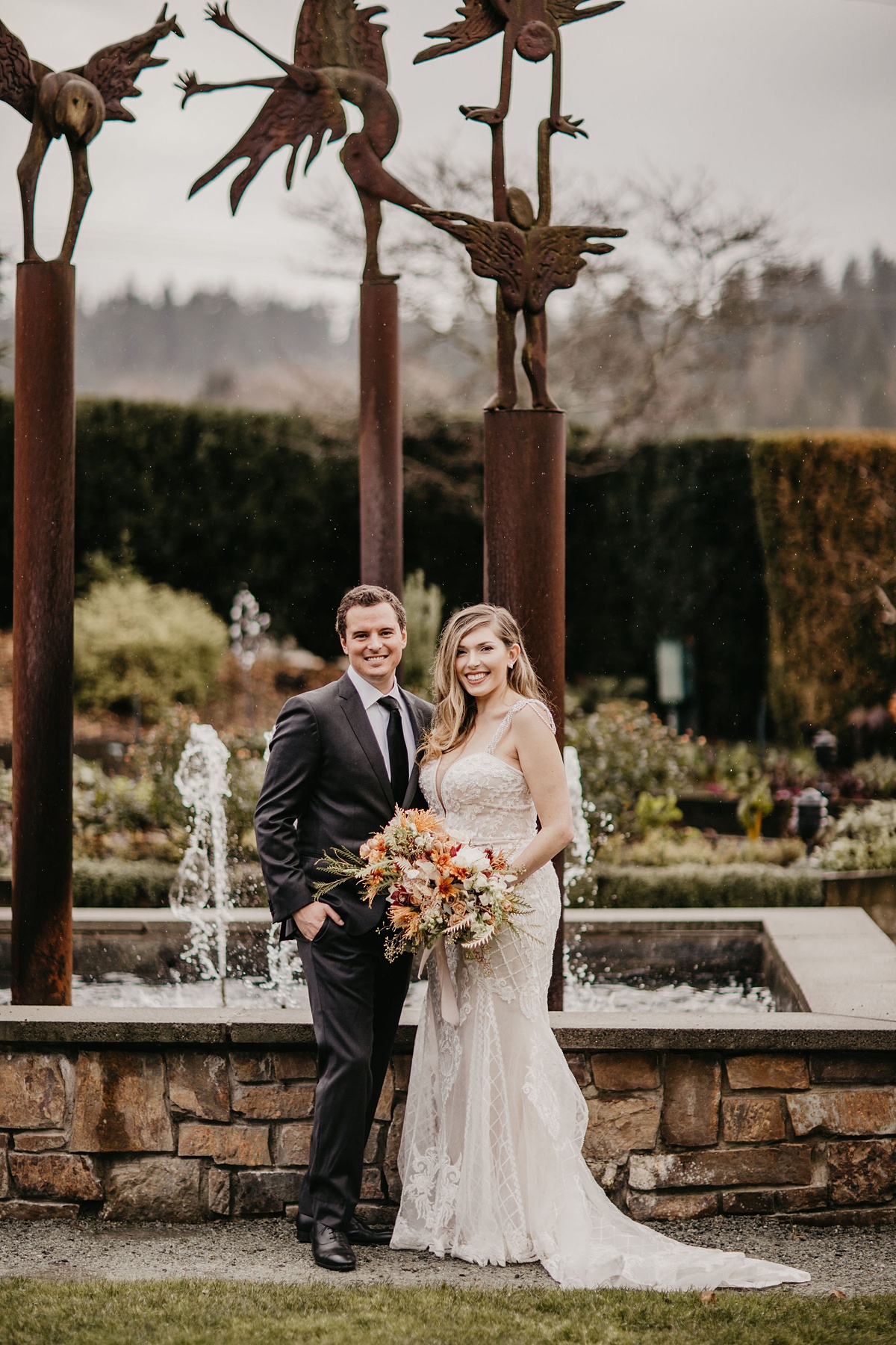 Willows-Lodge-Wedding-Bride-and-Groom-In-Front-of-Fountain the bride and froom standing and smiling in front of a garden fountain at the Willows Lodge
