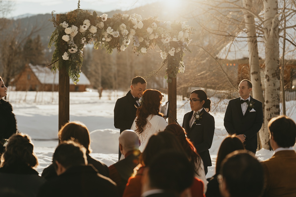 The couple saying their vows in front of wedding floral arch