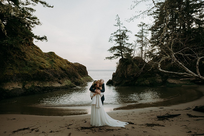 The couple embraces on the beach at sunset
