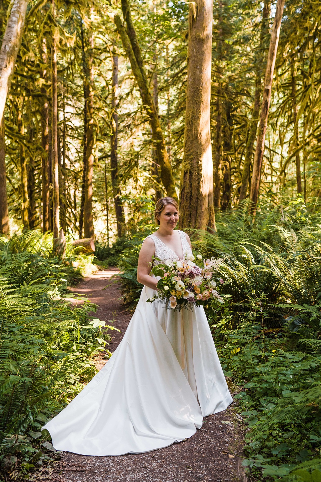 Mountain-Wedding-with-Vibrant-Summer-Blooms-Bride-in-Woods A bride holds her bouquet in the woods