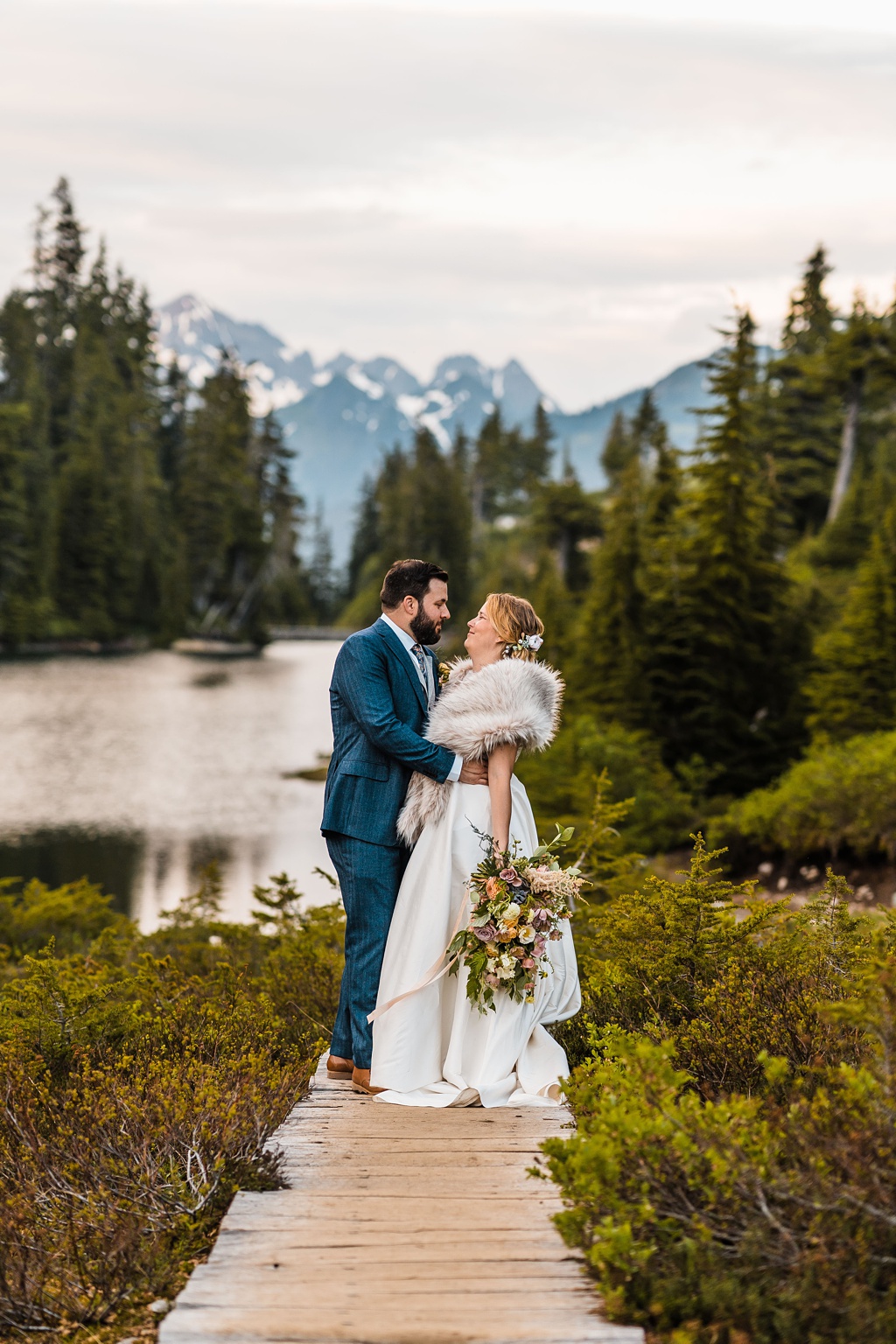 Mountain-Wedding-with-Vibrant-Summer-Blooms-Lakeside-Boardwalk The couple stands on a lakeside boardwalk