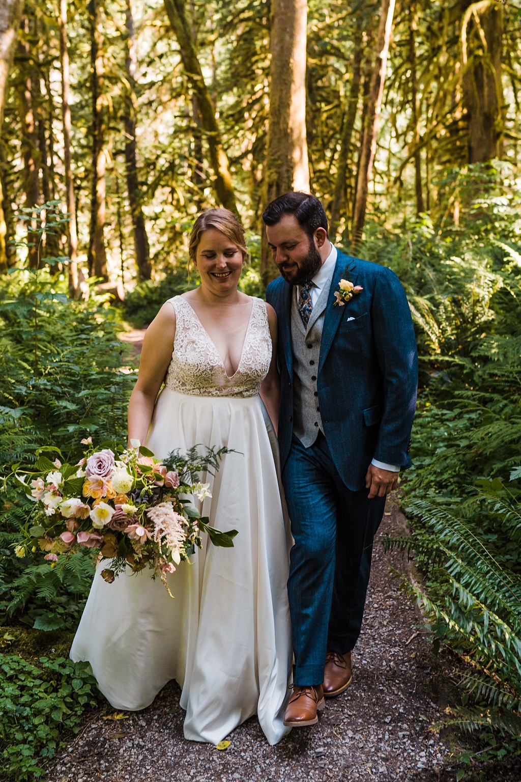 Mountain-Wedding-with-Vibrant-Summer-Blooms-Walking-in-Woods The couple walks in the woods holding the bouquet