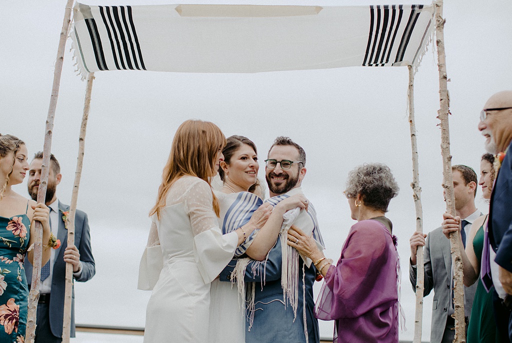 Bloom-Poet-Seattle-Wedding-Florist-Kiana-Lodge-Wedding-Chuppah The couple embraced by both of their mothers during the Jewish wedding ceremony at Kiana Lodge
