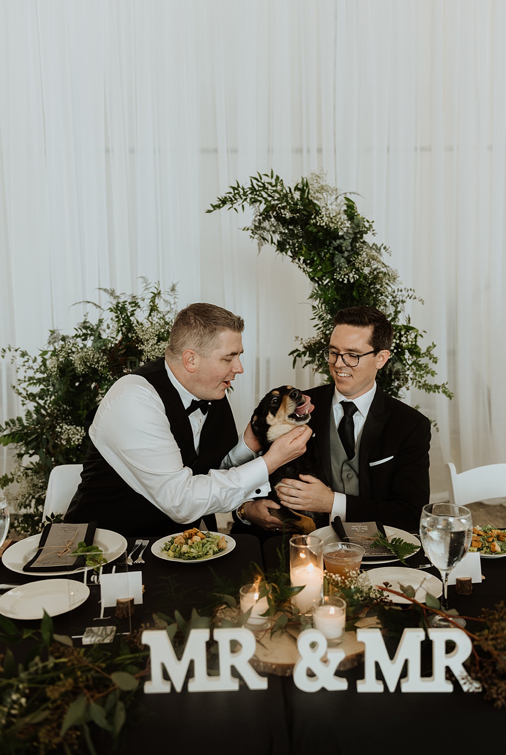 A gay couple smiles with their dog Maggie at the head table