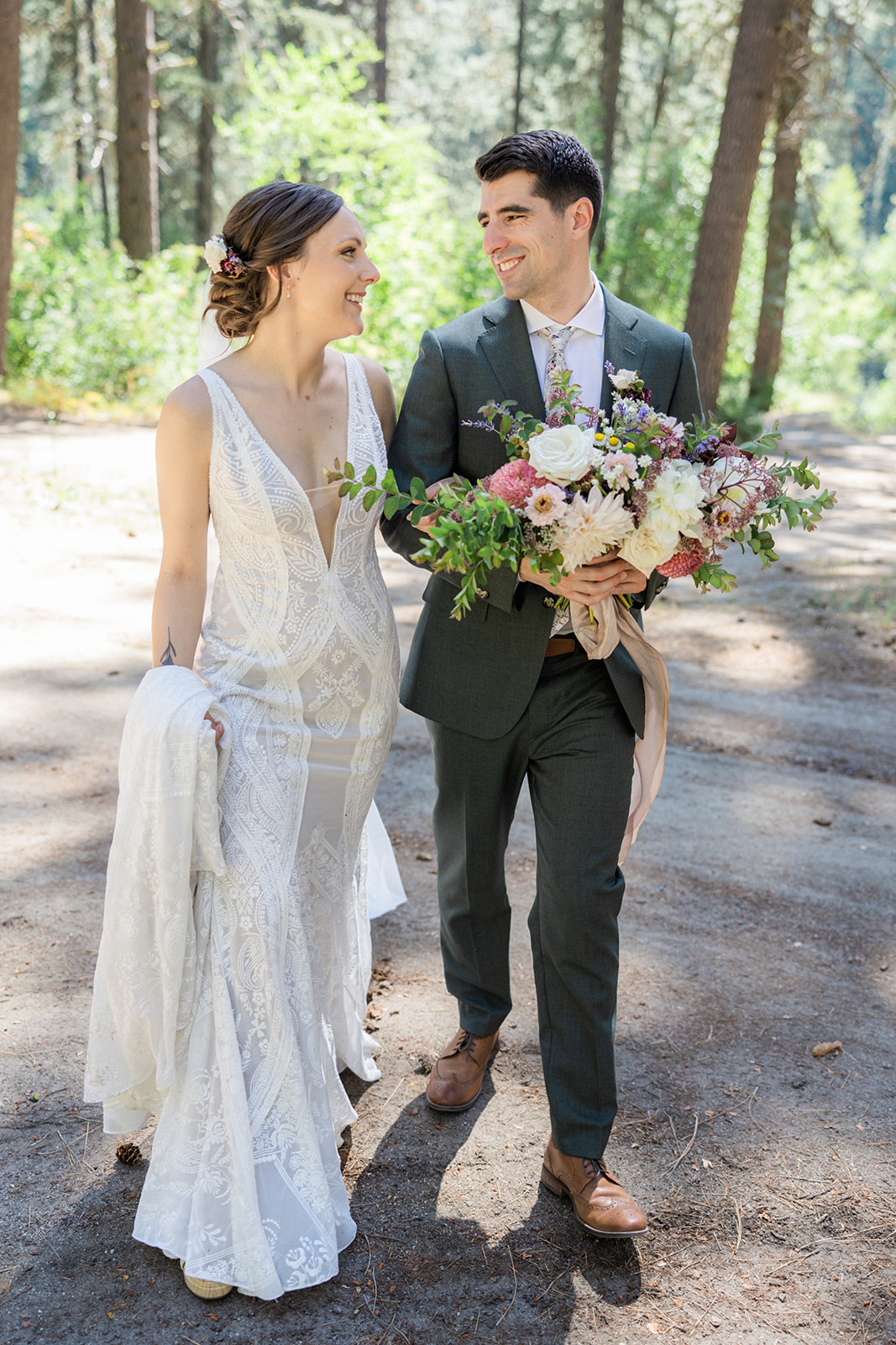 Nicole and Adam The bride and groom walk through the forest together, holding a bridal bouquet