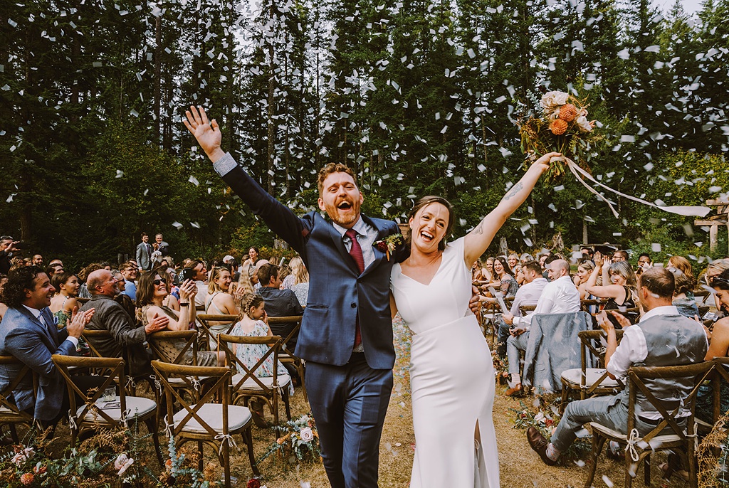 Bloom-Poet-Seattle-Wedding-Florist-Summer-Wedding-Confetti.jpg The couple walking down the aisle with "just married" smiles with confetti at their summer wedding